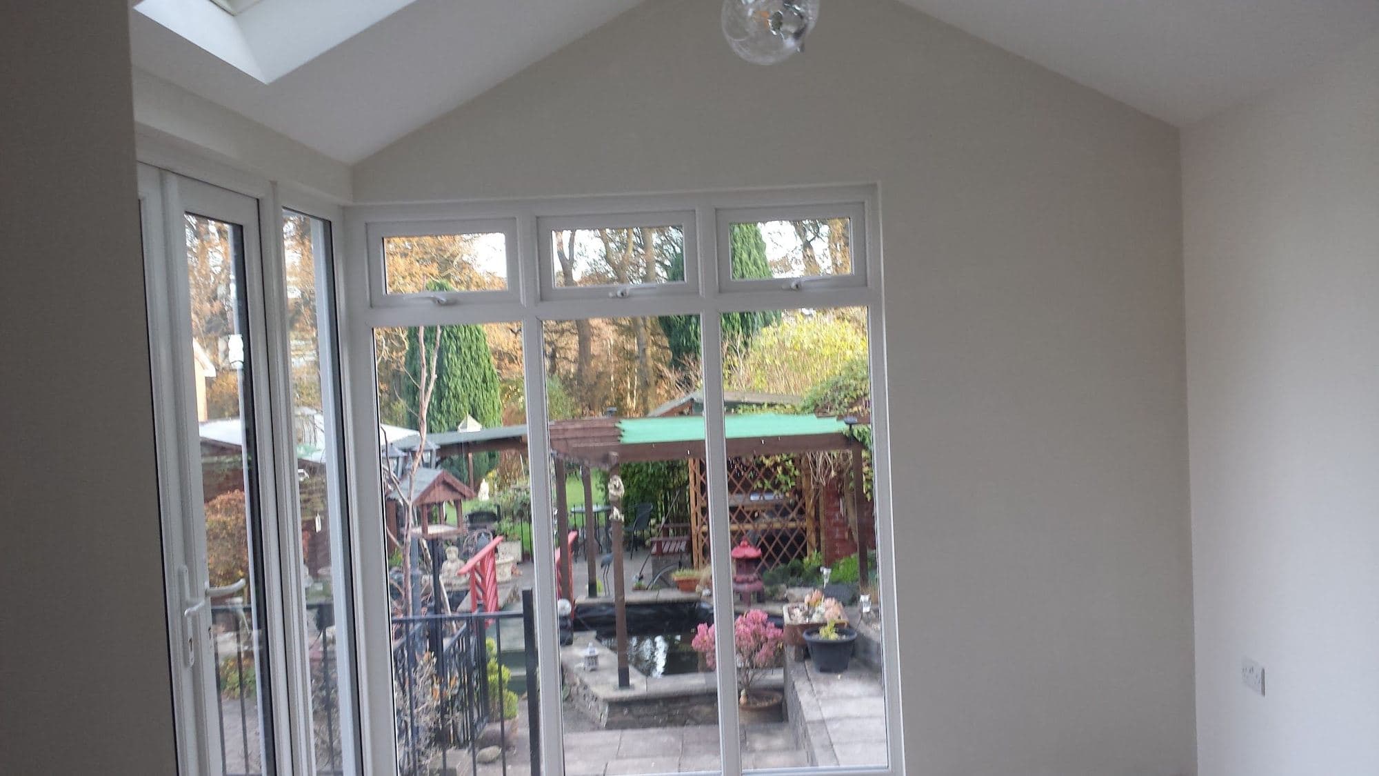 A bright new room with white walls, a pitched ceiling with a roof window, and white patio doors onto a garden