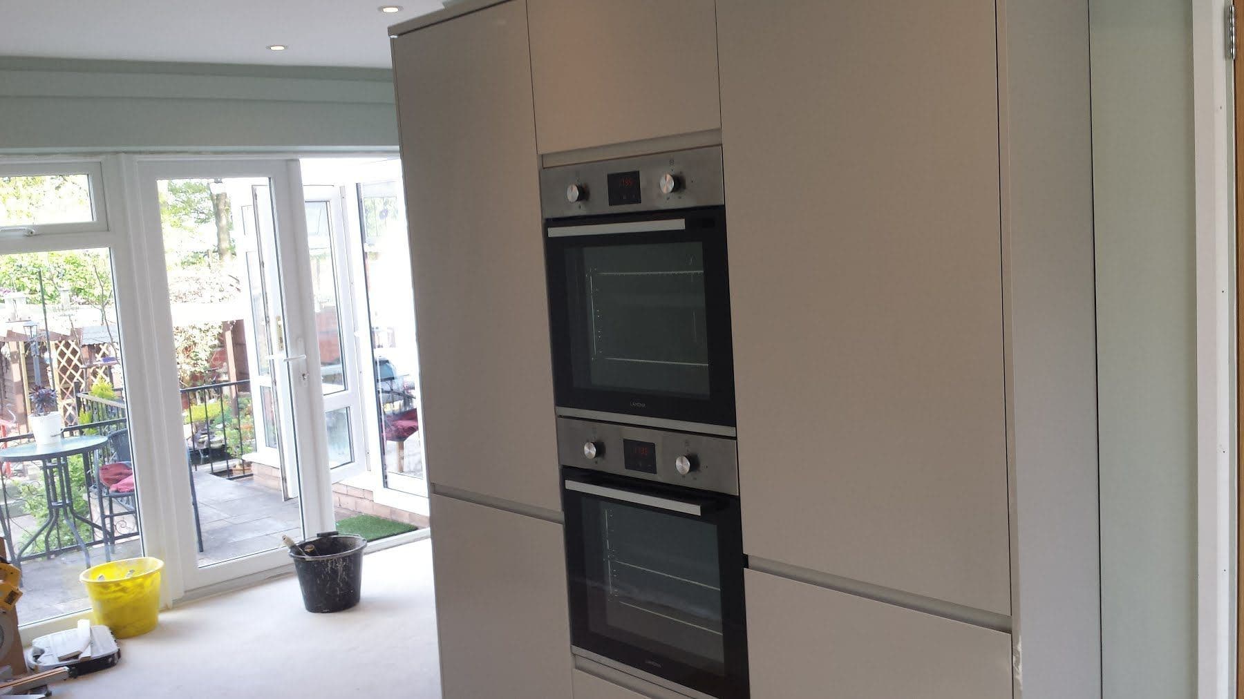 A fitted kitchen with tall cream units, a double oven and glazed doors onto a conservatory
