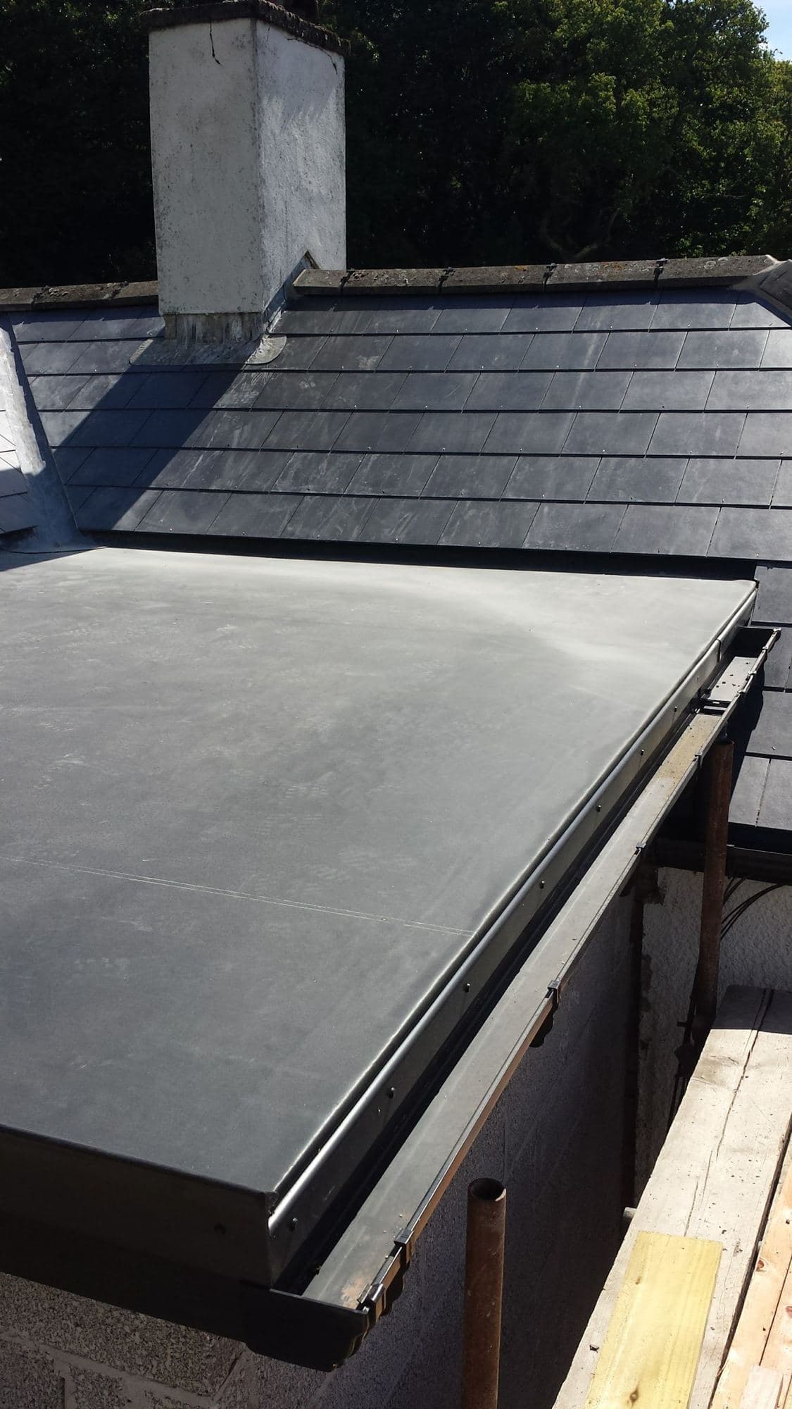 A flat roof with a smooth black covering next to a slate roof and a chimney