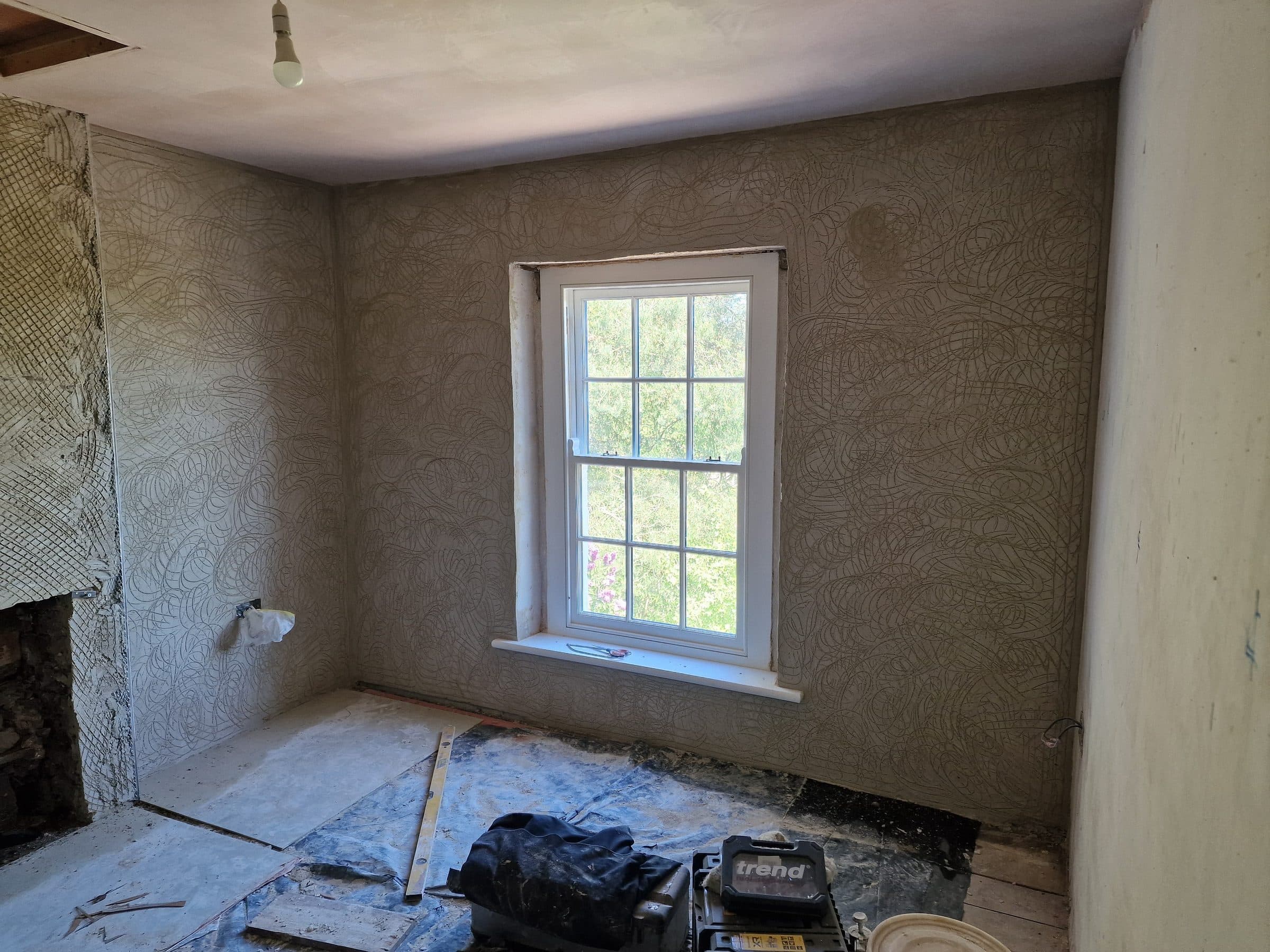 Lime plaster scratch coat on the walls of a cottage bedroom, around a sash window