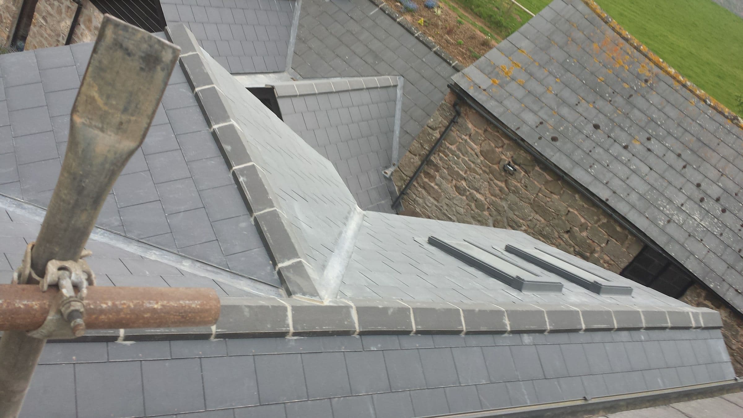 A new slate roof with lead valleys and two roof windows, seen from the scaffold, beside an older stone building