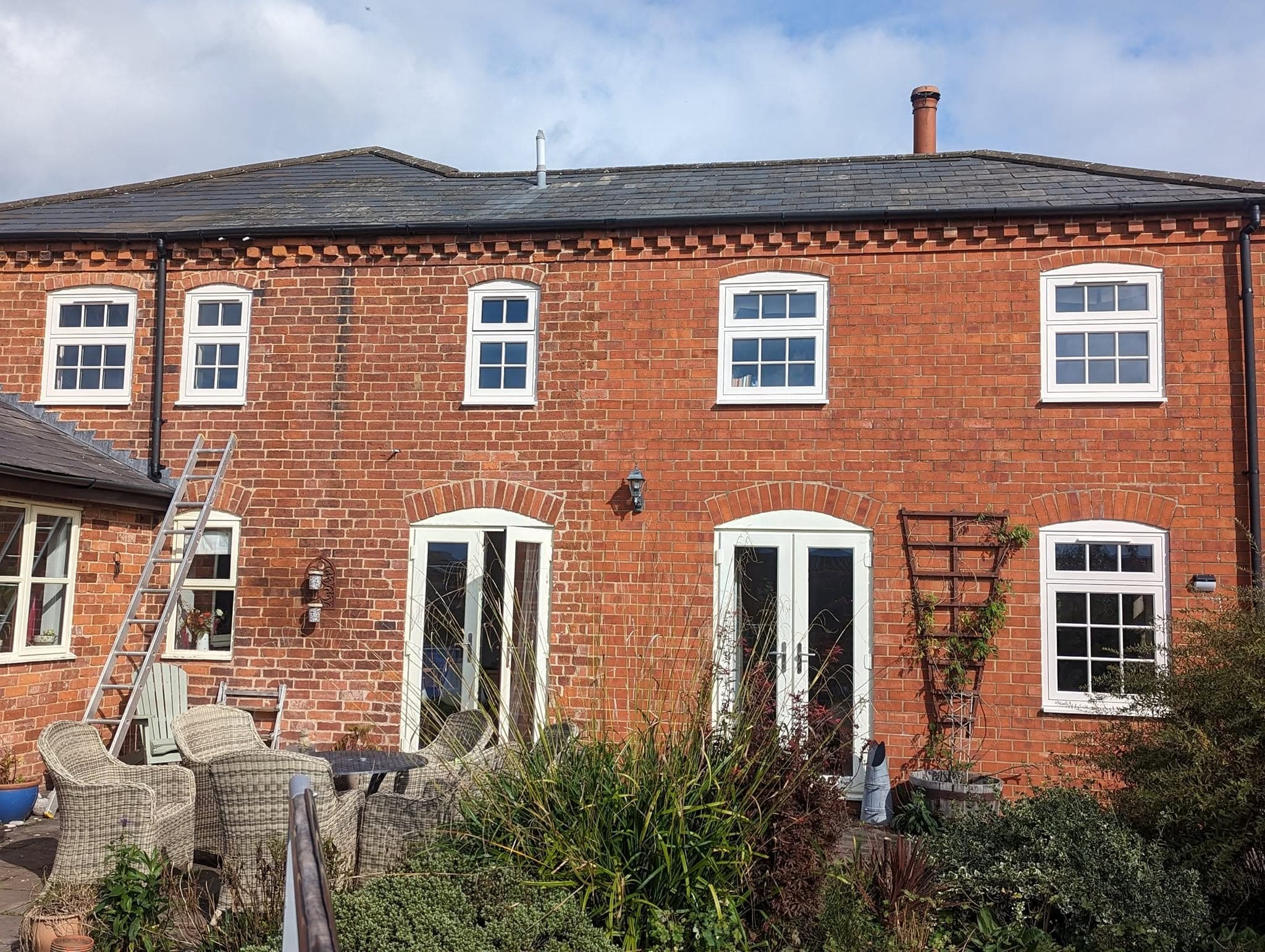 The back of a red-brick period house with white sash windows and two sets of french doors, with a ladder against the wall