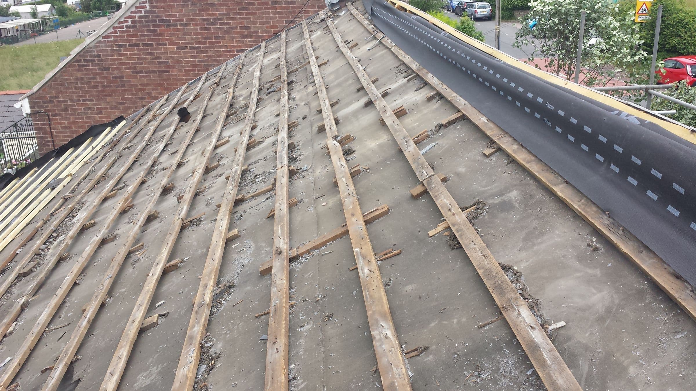 A roof stripped of its tiles back to the old battens and sarking, with new membrane along one edge