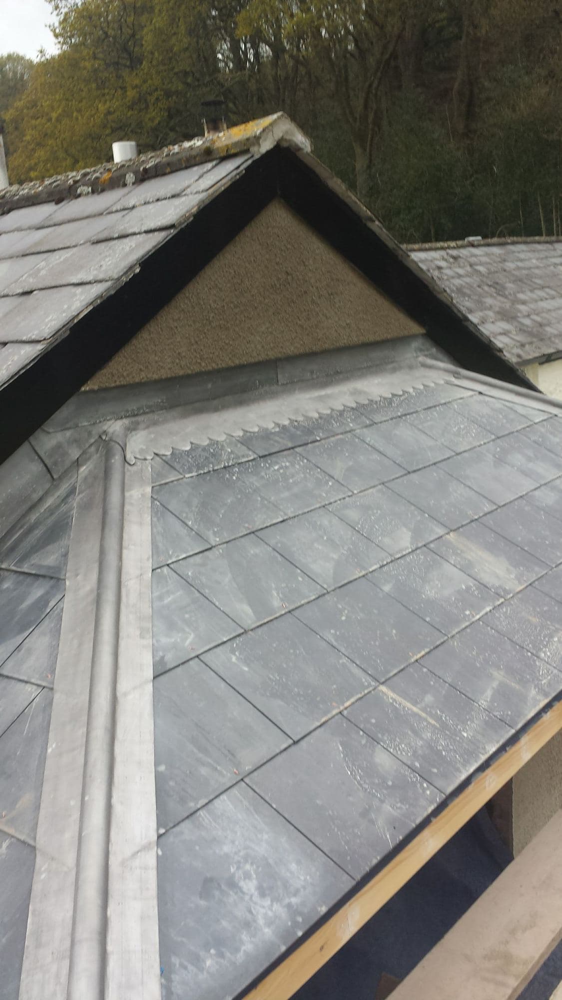A slate-clad gable end with lead flashing along the edge