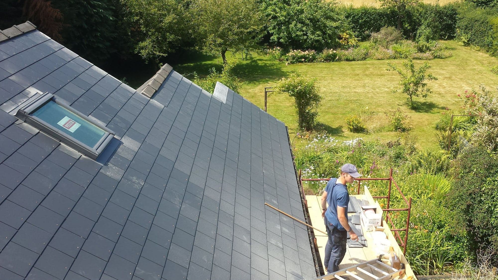 A new slate roof with a roof window, and a man working on scaffold boards beside it above a green valley