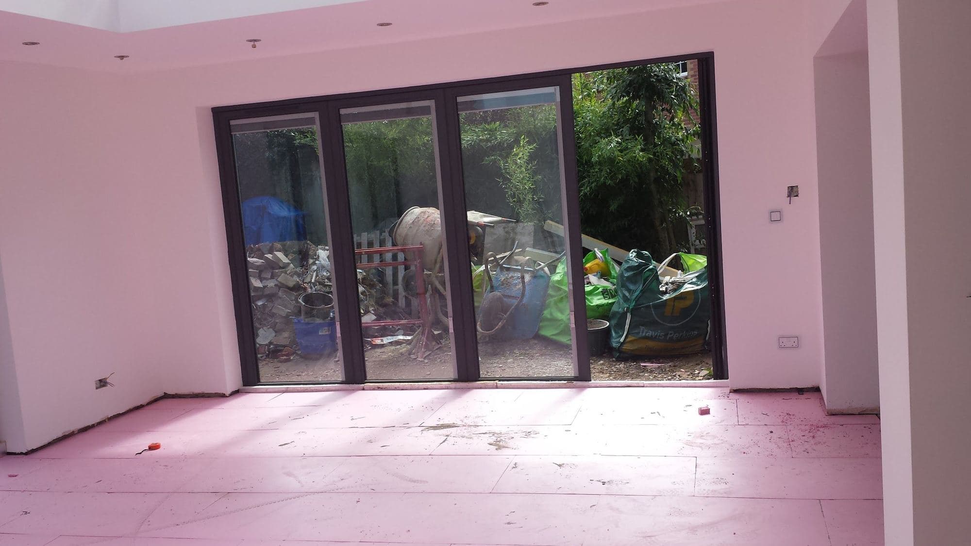 A new room with dark-framed bifold doors onto a garden and an insulated floor not yet finished