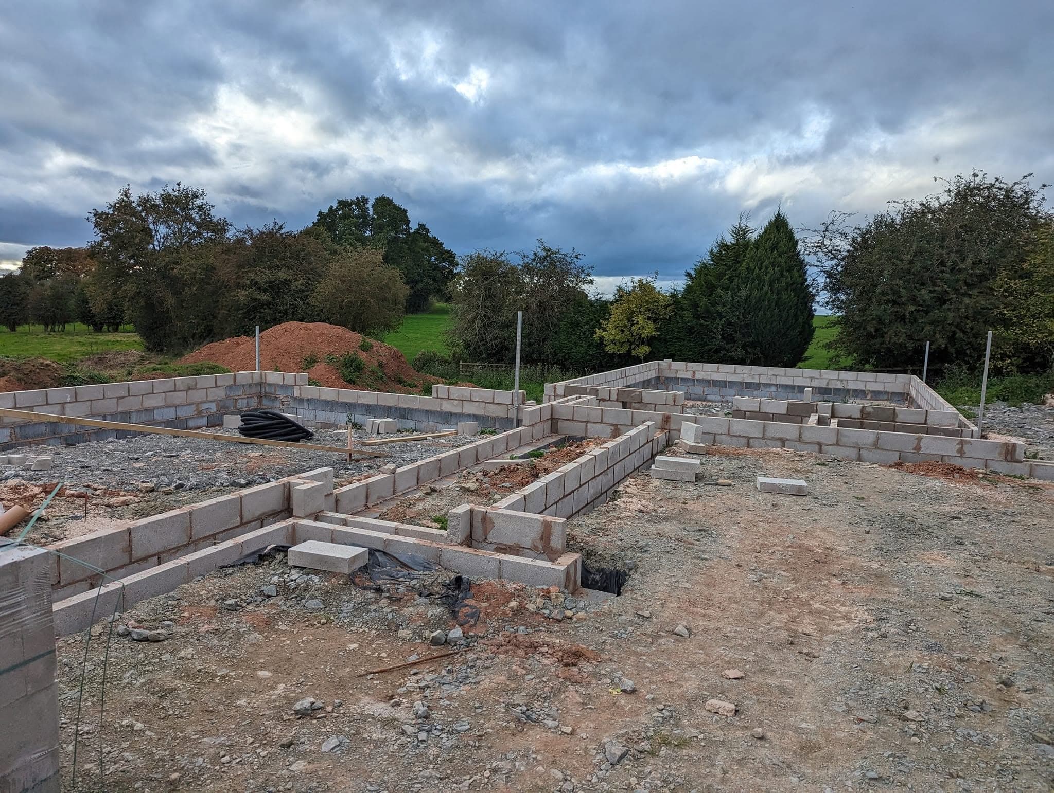 Block foundations laid out for a new building on a levelled site, with fields and trees behind