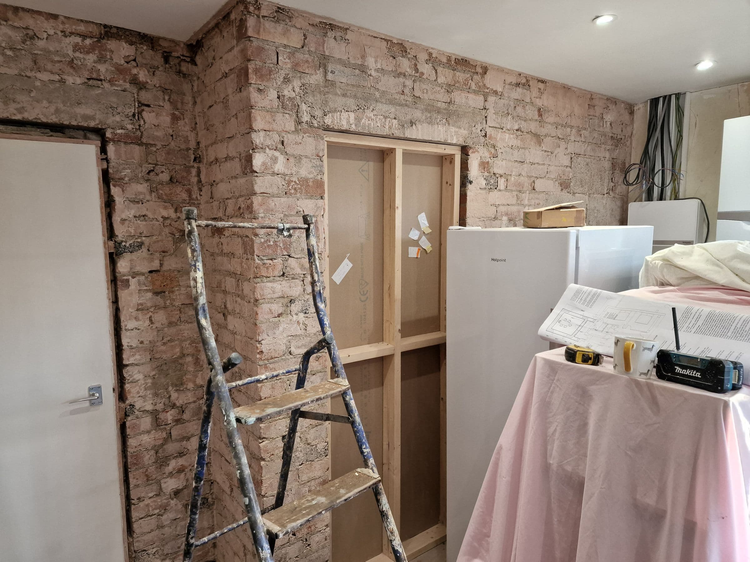 An old brick wall stripped of plaster, with a doorway framed out in new timber studwork
