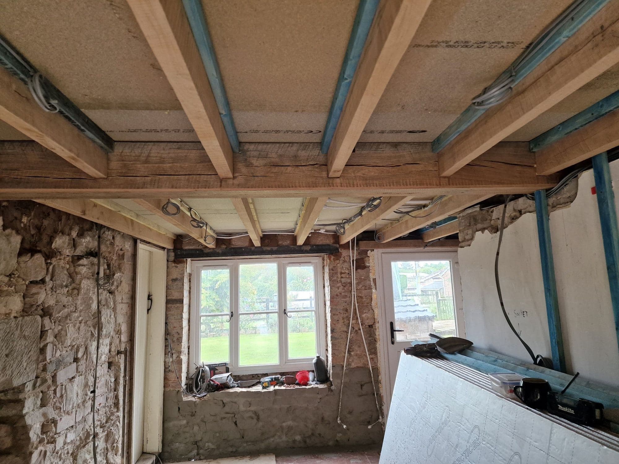 A stone-walled room with the ceiling opened up to the floor joists above and a casement window in the wall