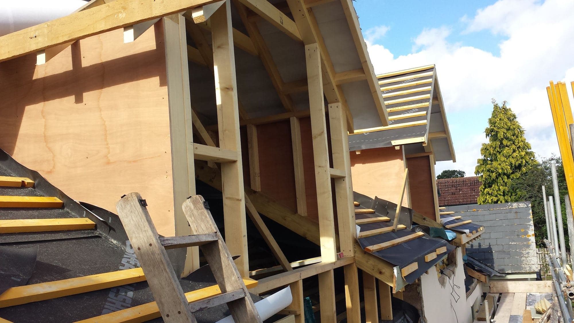 Timber framing and plywood sheathing of a dormer, seen from the scaffold, with a slate roof alongside