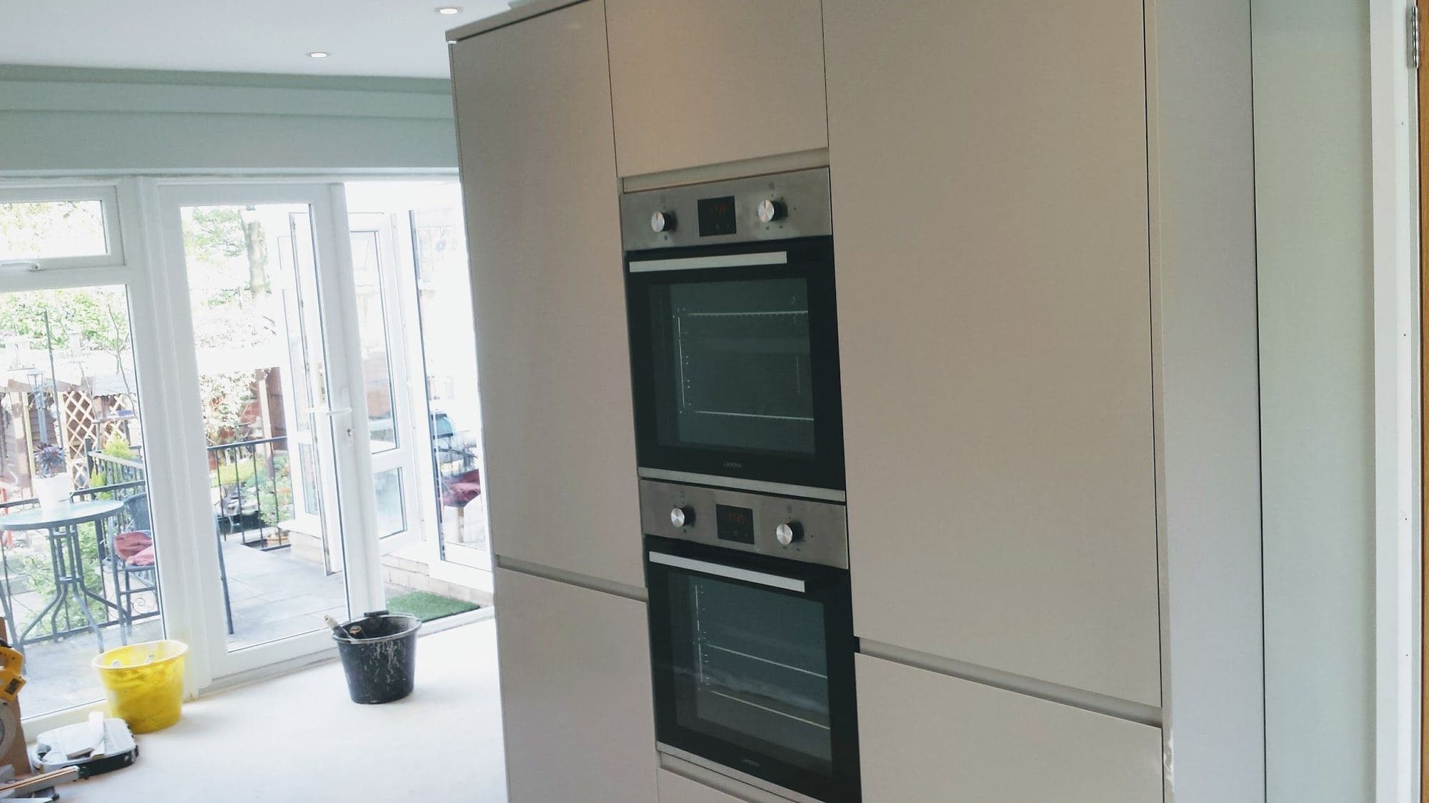 Tall kitchen units with a double oven beside patio doors that open onto a garden