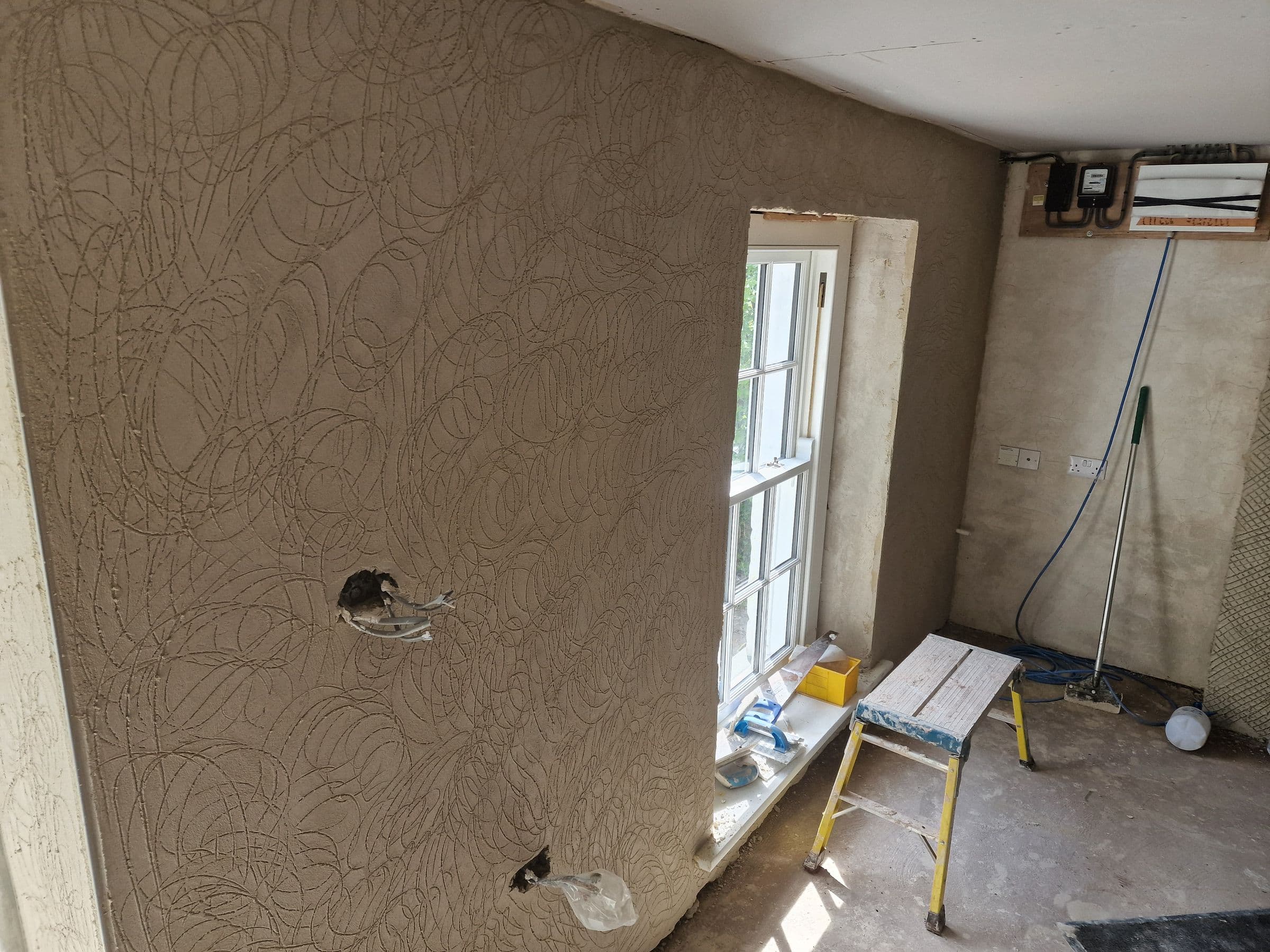 A wall of lime plaster scratch coat with its swirled key pattern, beside a sash window