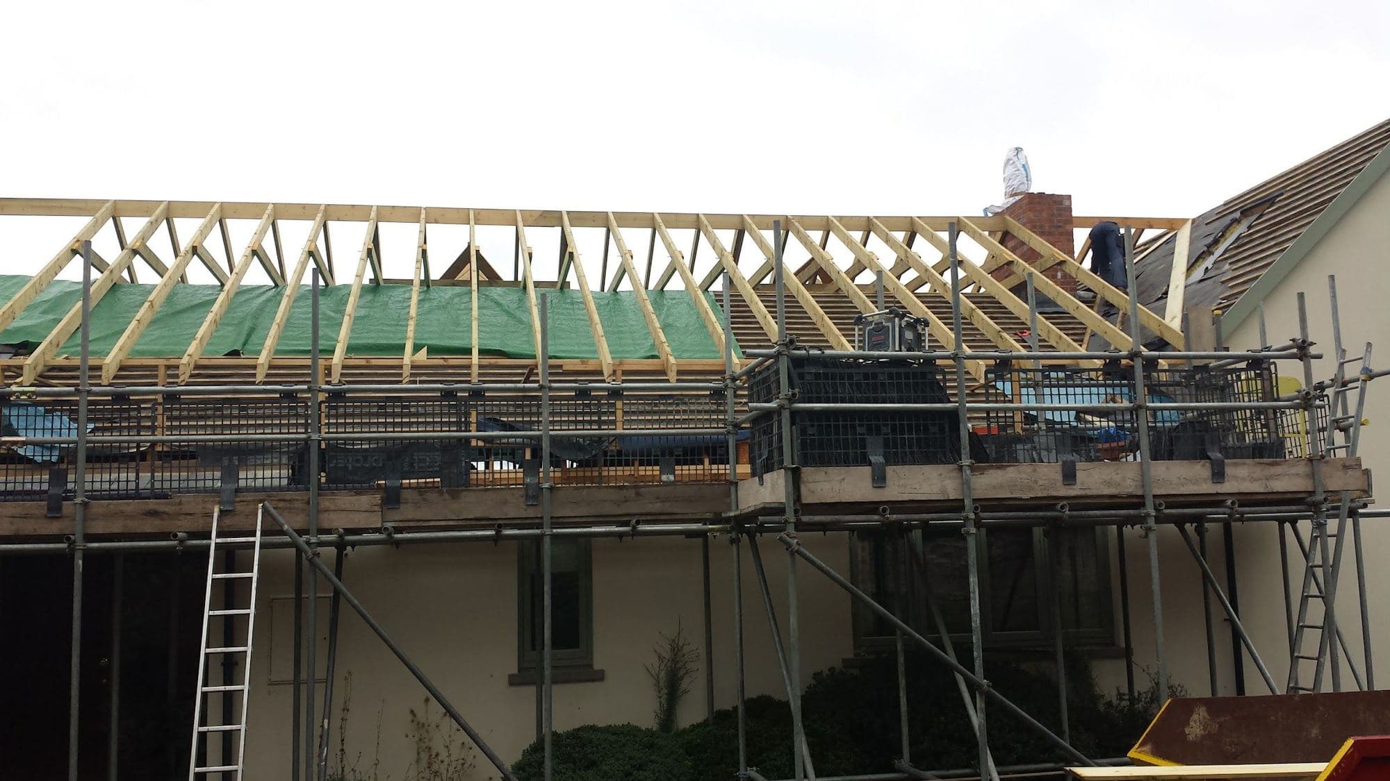 New roof timbers laid across a wide single-storey roof under scaffold, with membrane showing between them