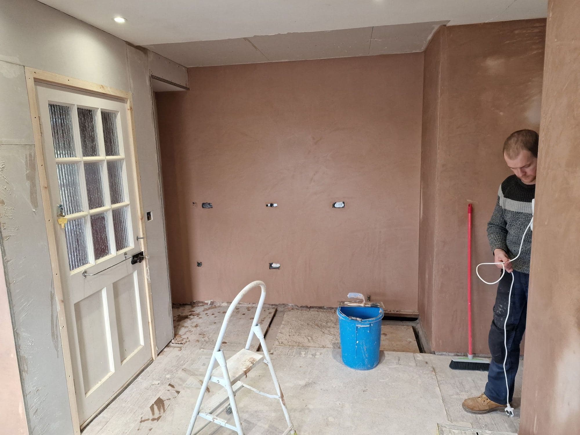 A man in a newly plastered room with a glazed door, a bucket and a stepladder
