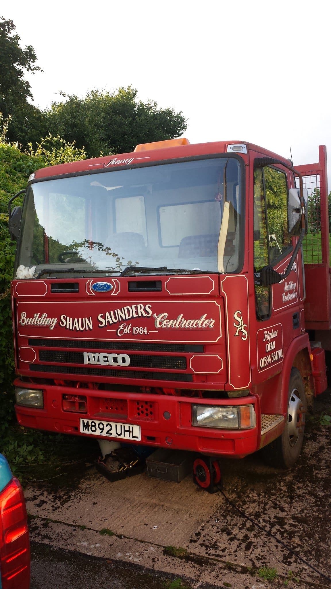 A red Iveco lorry signwritten 'Building, Shaun Saunders, Contractor', with the telephone number 01594 564770 on the door