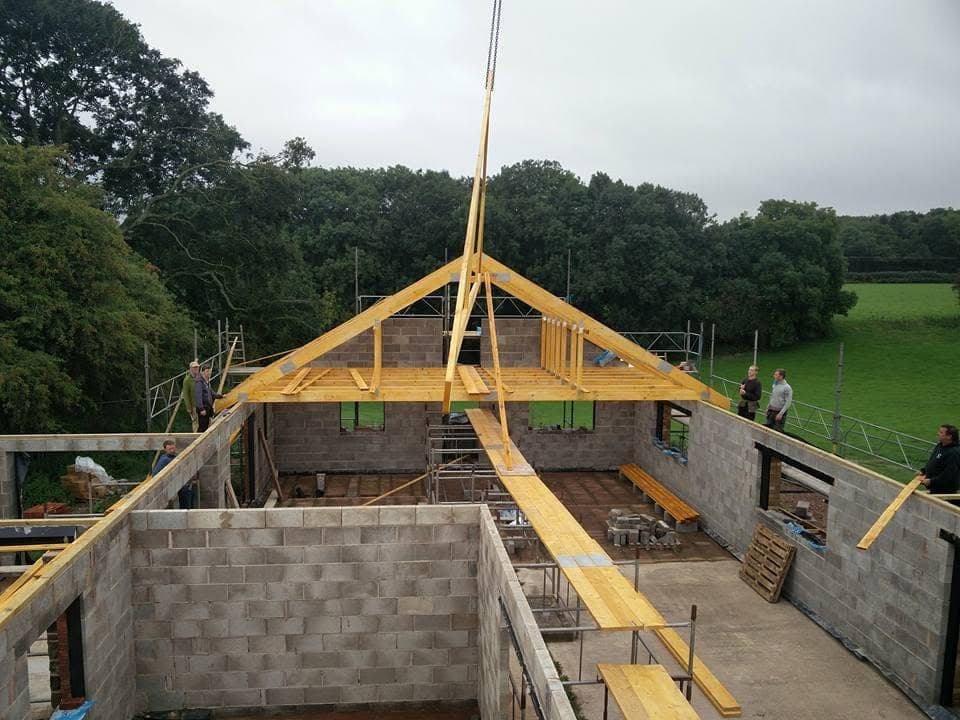 Timber roof trusses being lifted into place on the blockwork walls of a new building, with scaffolding around it