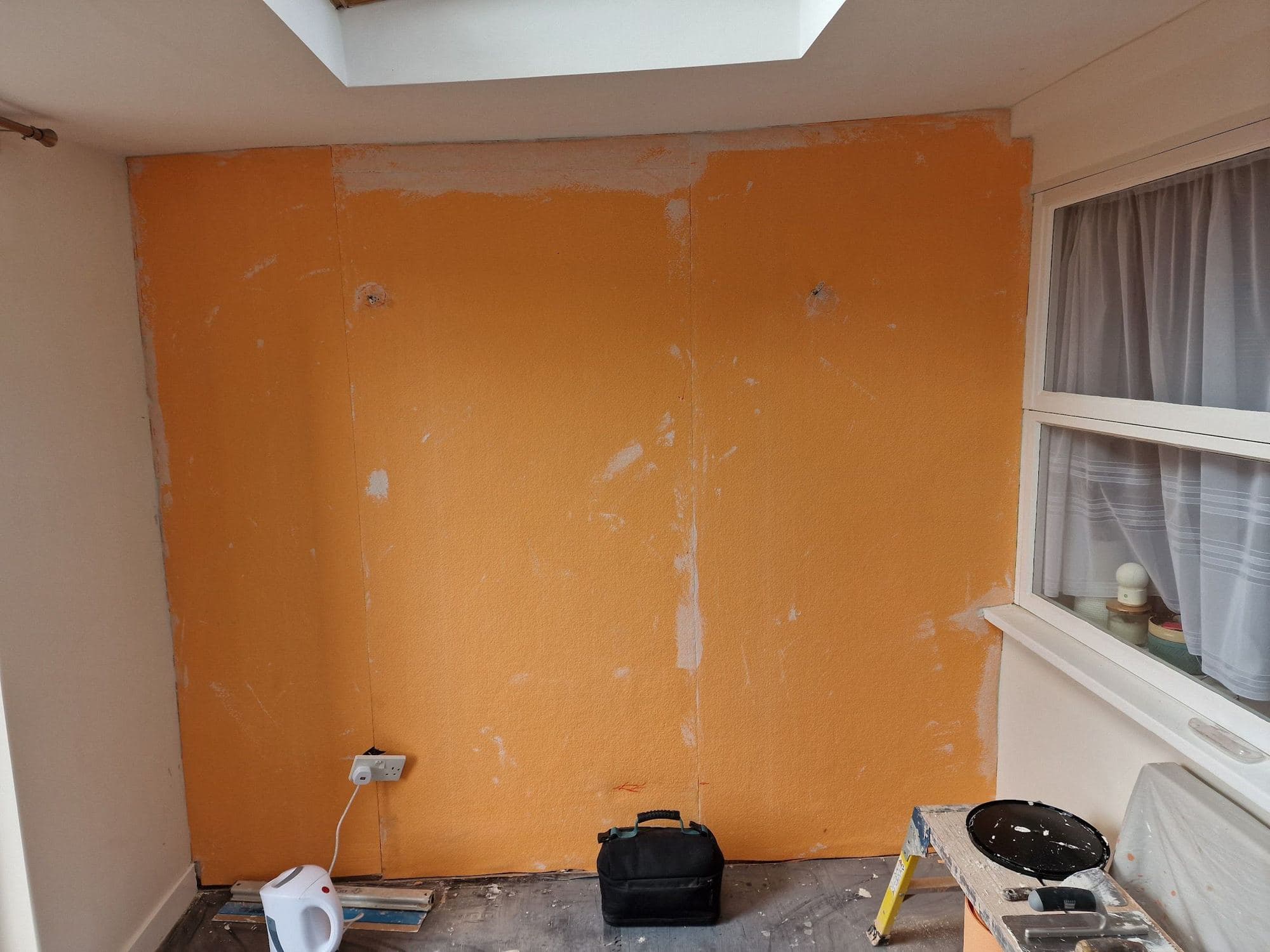 A room with a bright orange wall, a roof window and a socket ready for fitting out