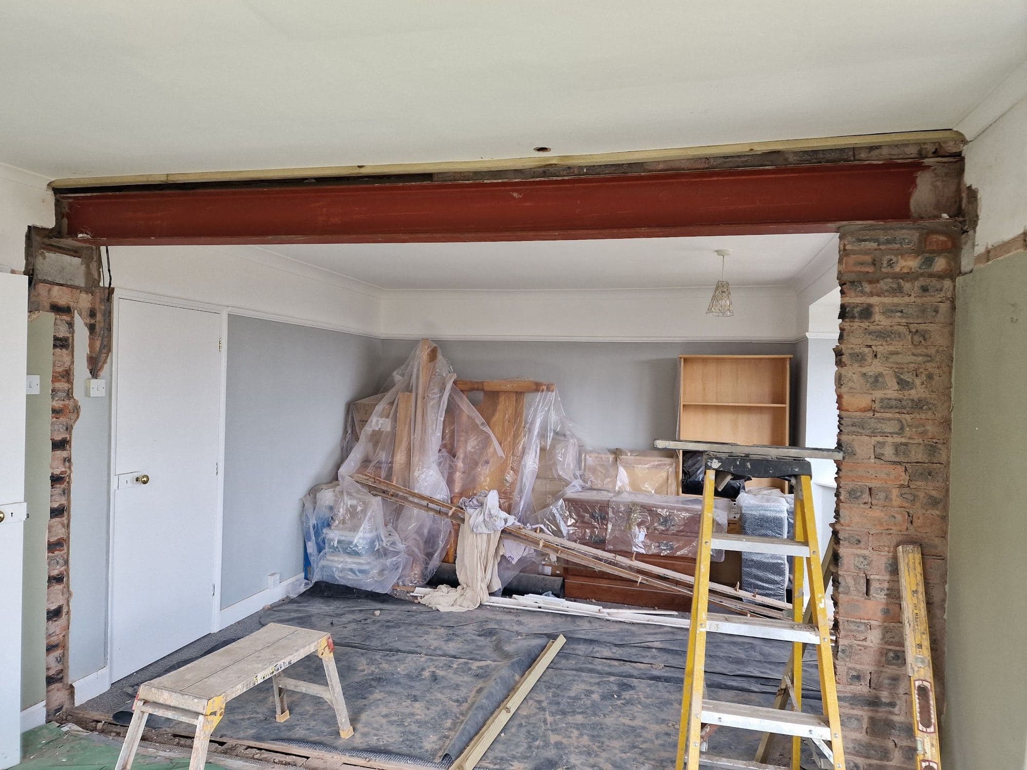A steel beam across an opened-up wall between two rooms, with dust sheets and tools below