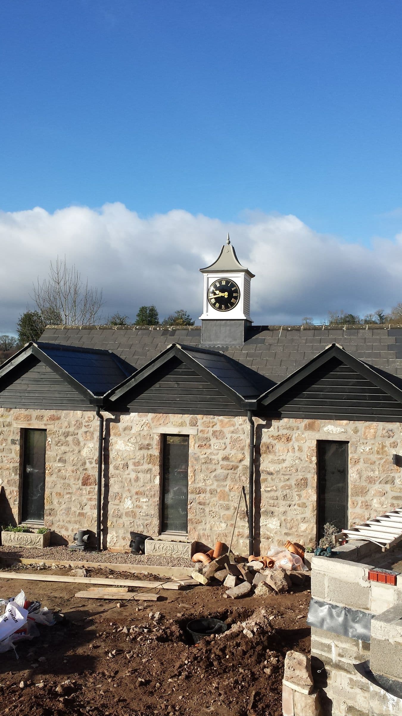 A row of stone-built units with slate roofs, gabled dormers and a white clock turret, under a blue sky
