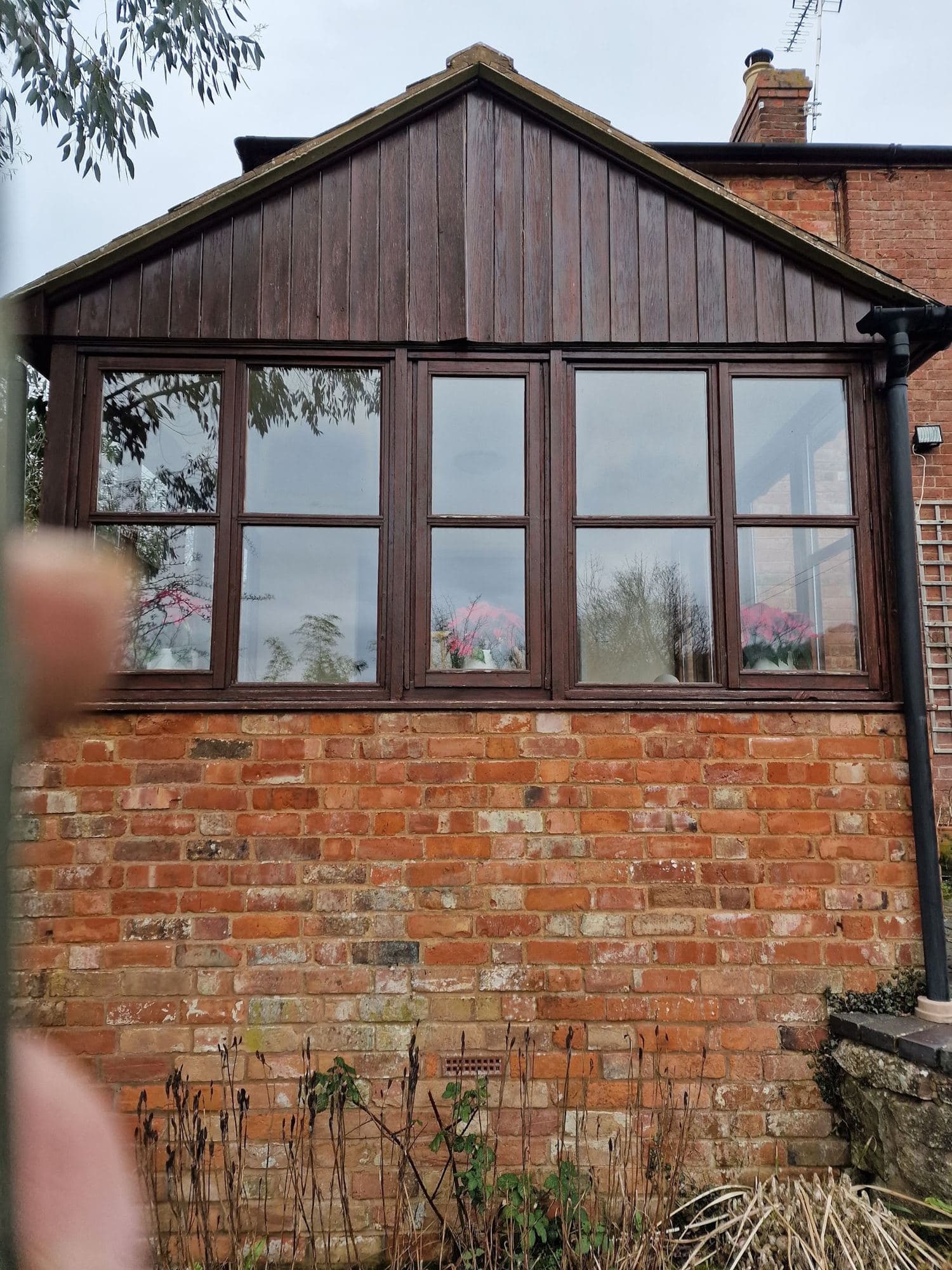 A timber-clad gable over a row of dark wood window frames on a red brick wall