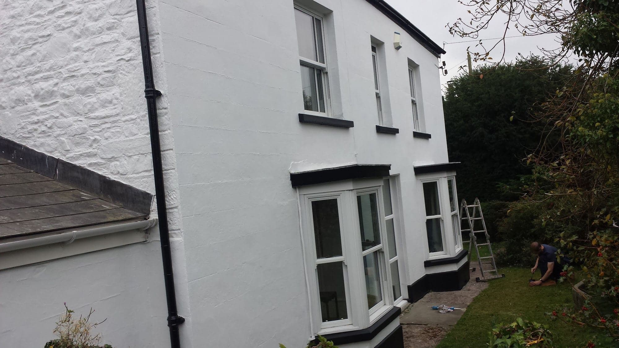 A white-rendered cottage wall with sash windows and a green-painted frame