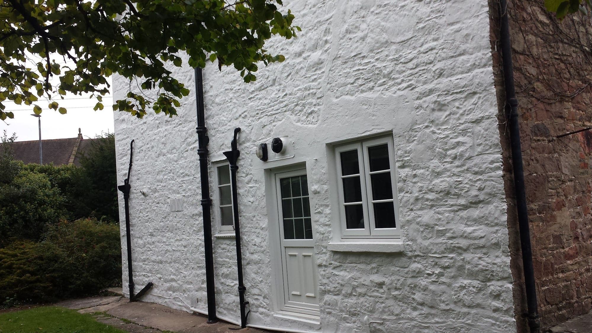 A white-rendered stone cottage wall with a panelled door, a small window and a dark downpipe